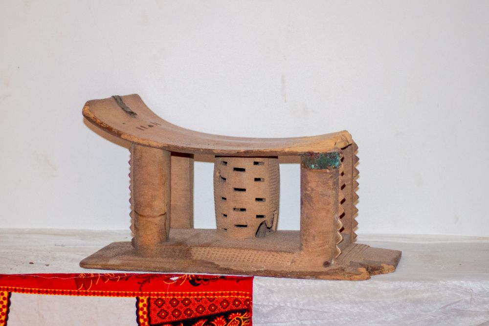 A worn carved stool with metal repair at one column