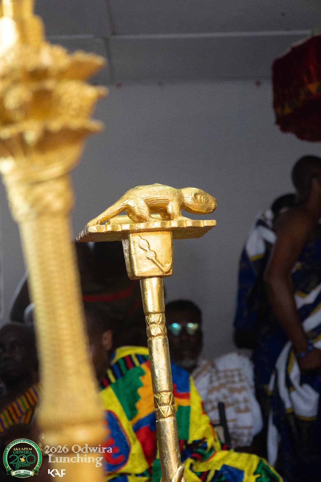 A gold chameleon finial on a linguist staff, held above the crowd